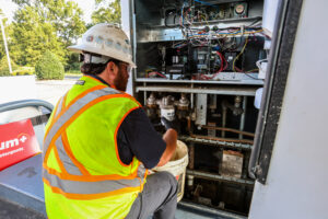 A technician in full PPE performing compliance inspection changing the filters in a under dispenser sump at a fuel station