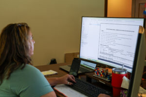 A female compliance employee works at her desk completing a State of Georgia Annual Underground Storage Tank Registration Form on the computer.